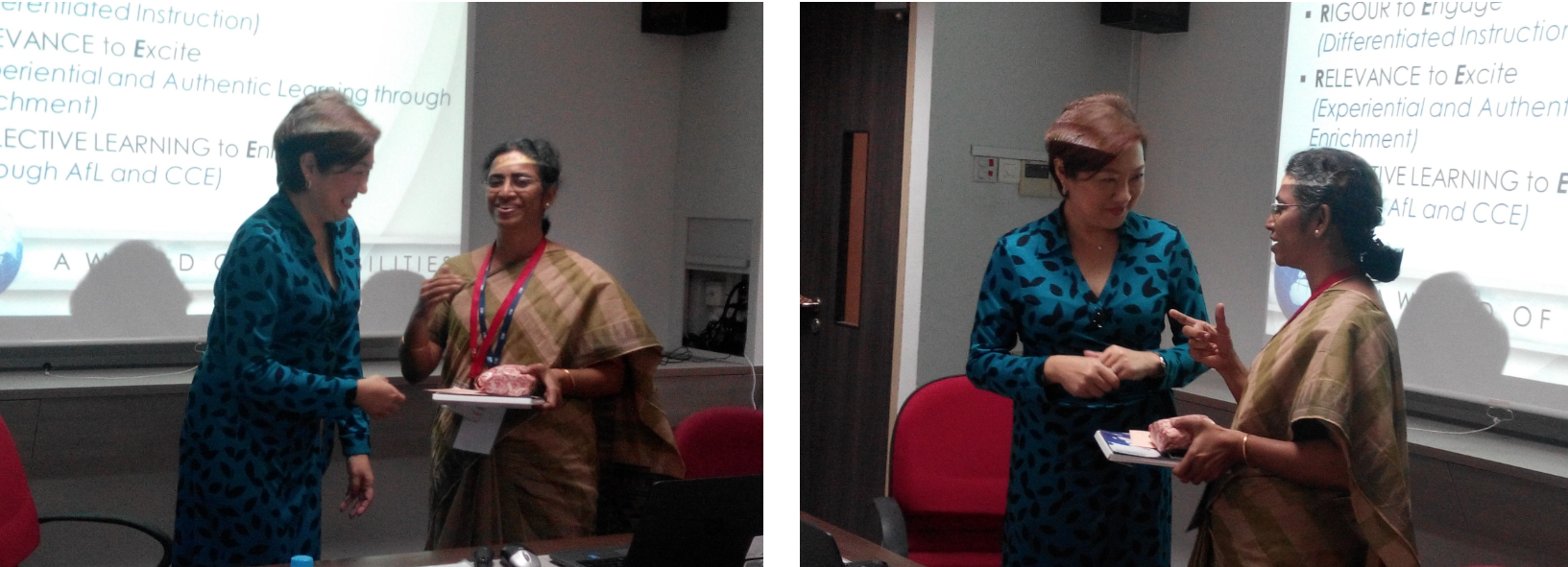 Two women in a conference room exchange a gift near a presentation screen showing educational bullet points.